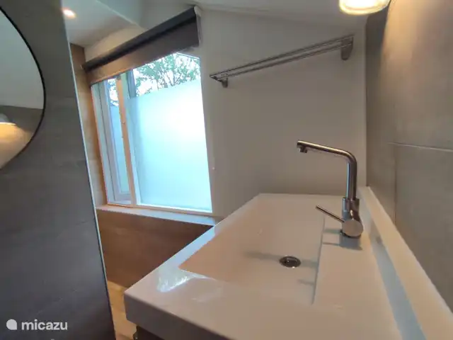 De badkamer heeft een grote spiegel. Daarnaast zorgt het rolgordijn voor nog meer discretie.